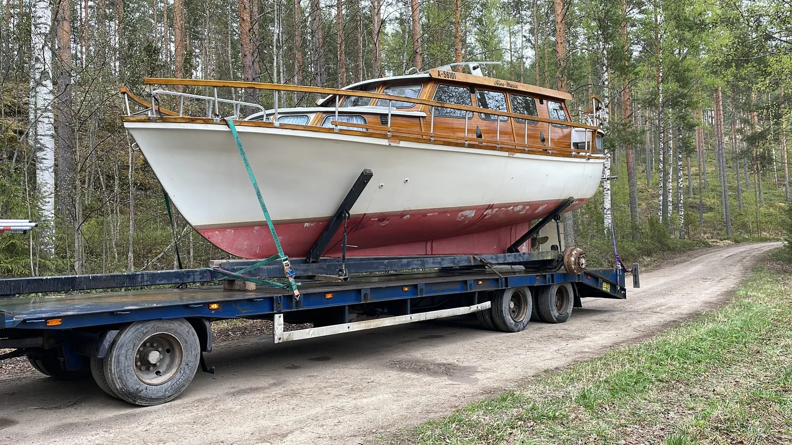 Mahonkikantinen puuvene nosturiauton lavalla metsätiellä.